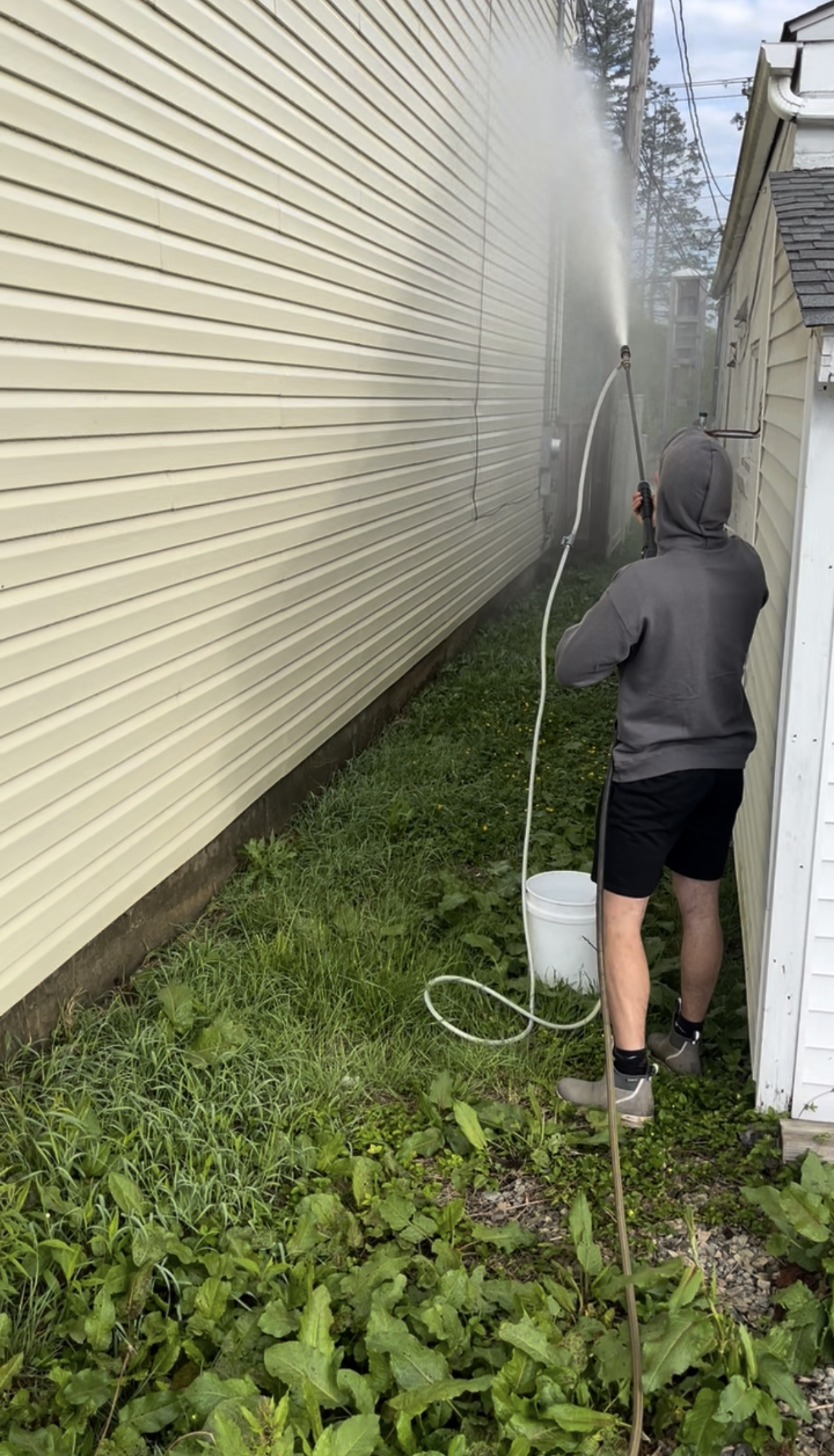 DeMoss technician soft-washing siding along the side of a house