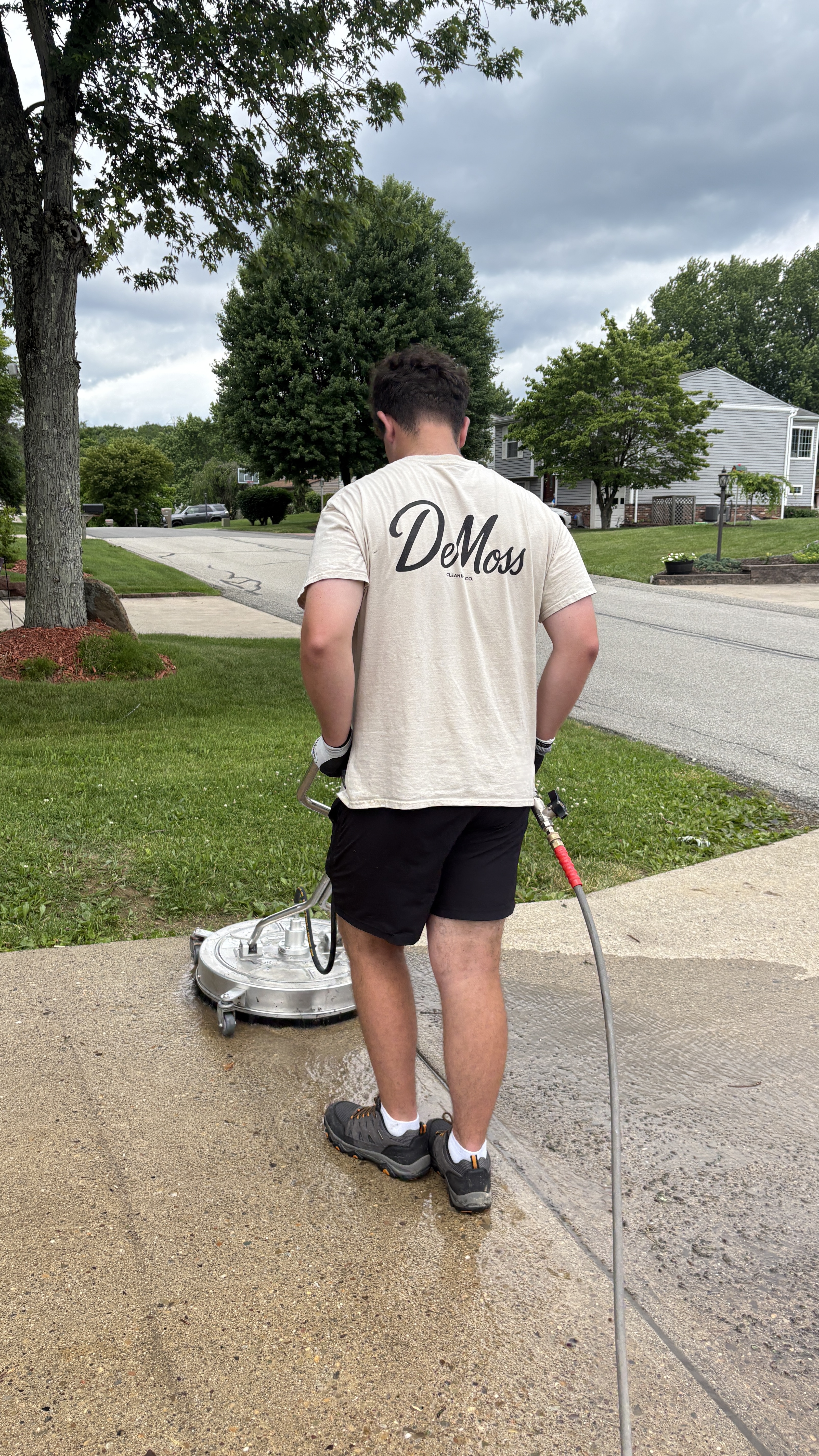 DeMoss technician surface-cleaning a concrete driveway with a pressure washer